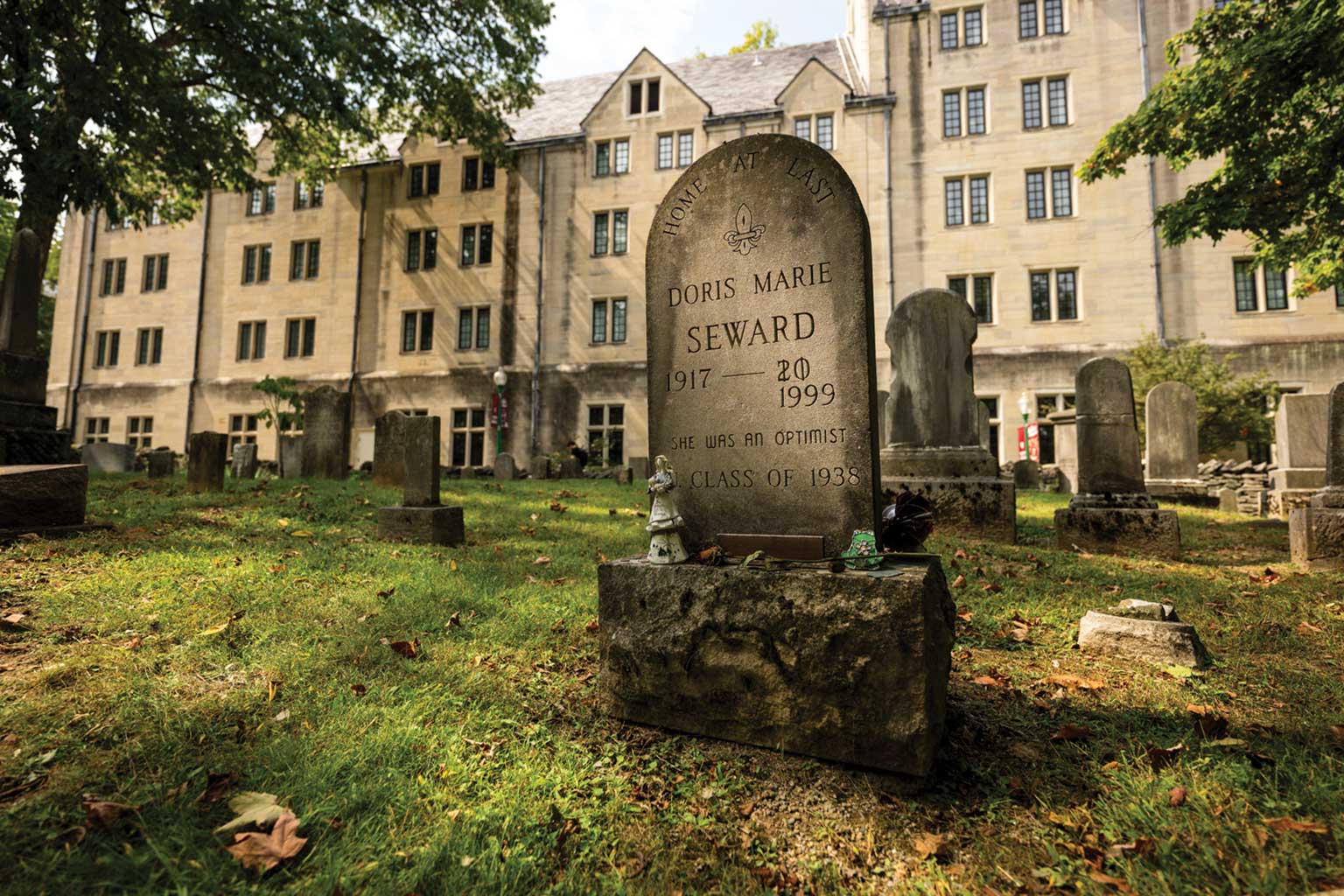 The gravestone of Doris Seward is in Dunn Cemetery on the Indiana University Bloomington campus with the Indiana Memorial Union in the background. The death date was originally recorded as two numbers, a two and a zero. Both are crossed out and 1999 is carved in. Below, the stone reads, "She was an optimist." Photo by Marc Lybrek.